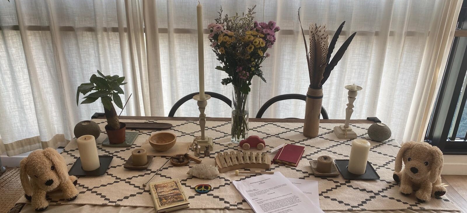 A blessing table set with candles, flowers, feathers, a wooden xylophone, a small red toy car and two soft toy puppies