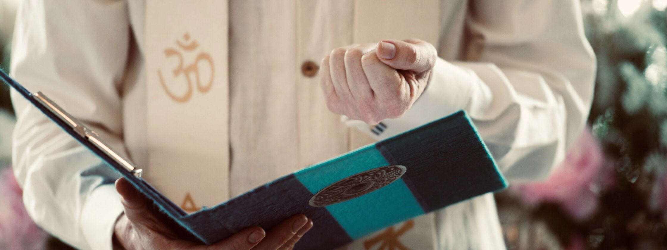 Peter's hands holding a ceremony book, wearing an interfaith stole