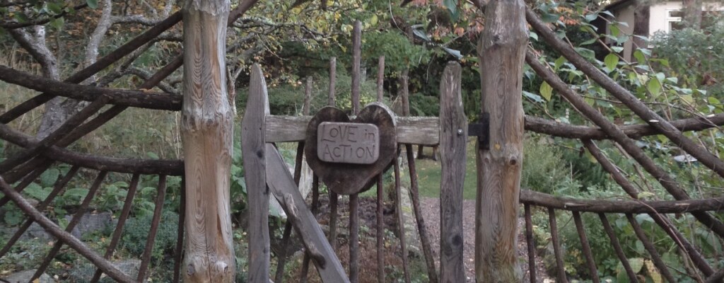 A hand-built wooden garden gate with a heart-shaped sign reading Love in Action
