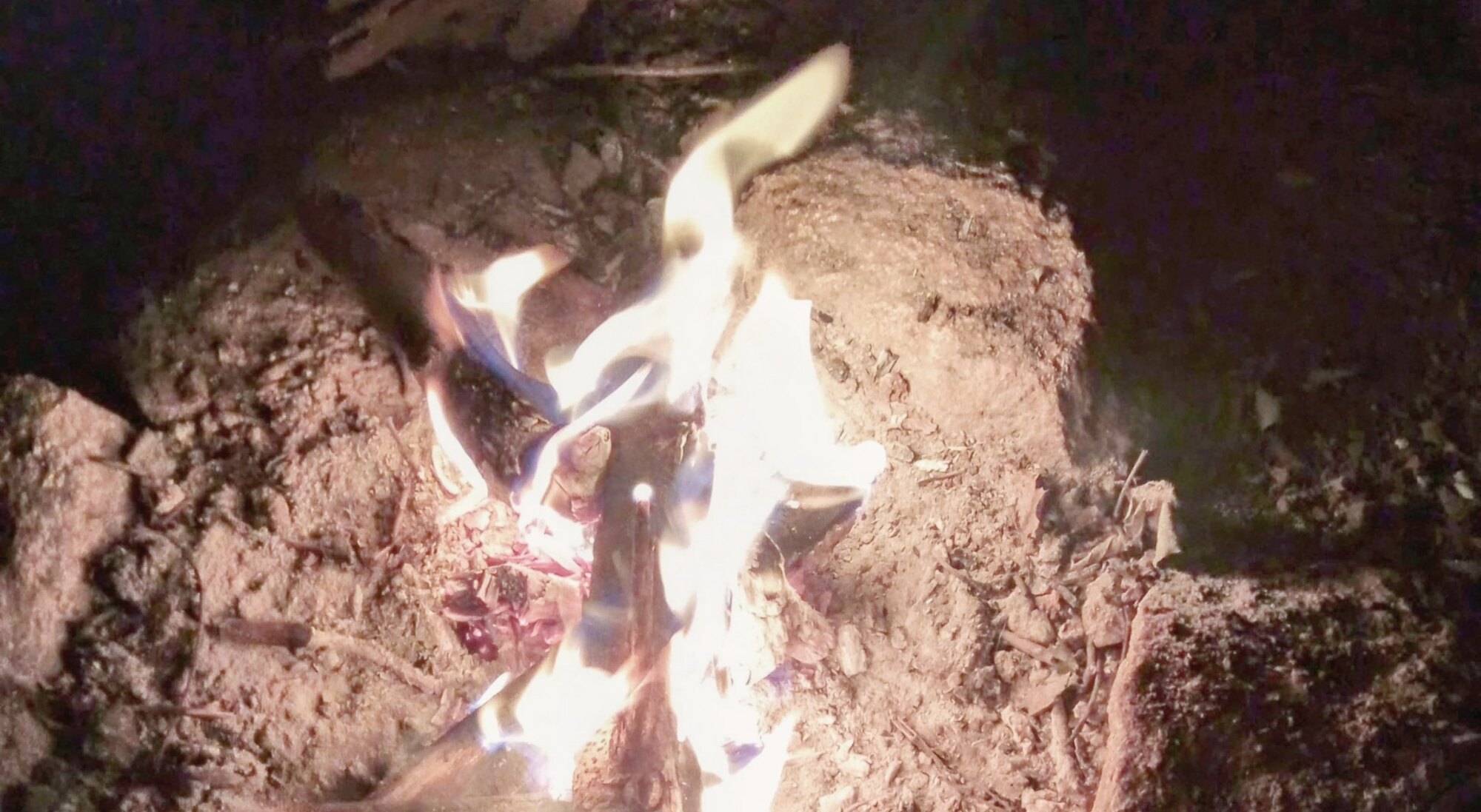 A small fire burning on bare earth at night